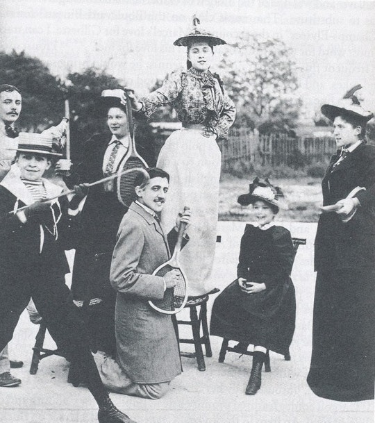 Grupo de pessoas posa para foto com Proust de joelhos fingindo tocar uma raquete de tênis como se fosse uma guitarra. Fonte